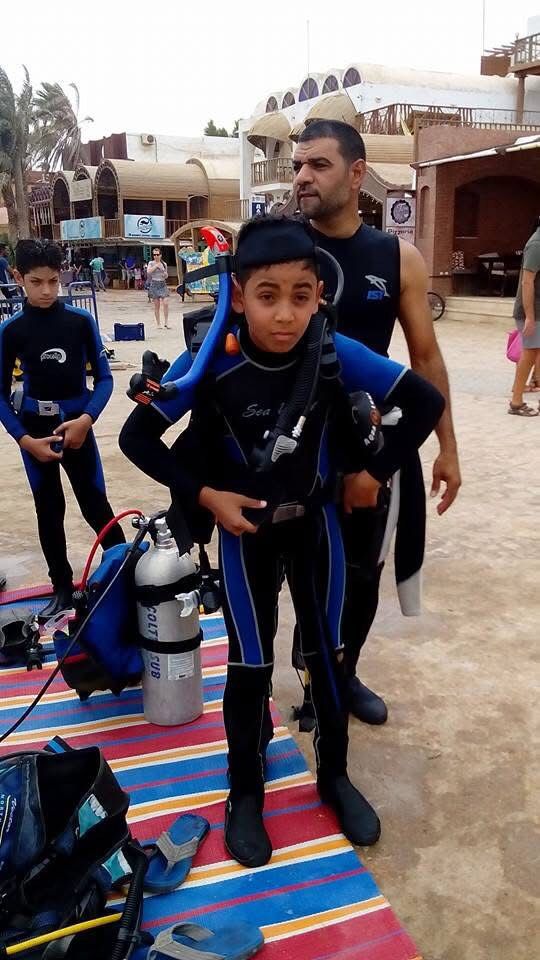 A young diver being geared up with a scuba tank on the Dahab promenade, other children in wetsuits waiting nearby